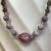 A beaded necklace in shades of purple featuring a center shell bead
